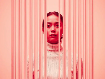 high resolution photography, front central profile, woman facing front, gaze to front, wearing a white turtleneck sweater, photographed entirely through thick vertically reeded architectural glass, vertical grooves running top to bottom across the entire frame, parallel vertical lines clearly visible, full-frame optical distortion dominating the image, acrylic glass in the foreground textured, realistic physical light refraction warping the profile of the face and upper body into vertical repetitions, subtle light softly radiating from the clothing and gently bleeding into the glass ridges, faint light scattering through the vertical grooves, low-key studio background in pale off-white tones, cool neutral lighting, restrained and minimal, realistic physics --ar 9:16 --raw --stylize 400
